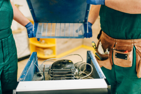 Technician repairing a jammed trash compactor in La Verne CA under a kitchen counter