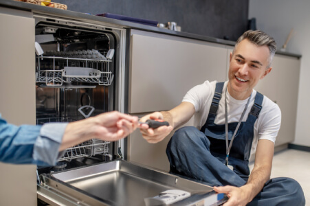 Appliance repair technician inspecting a dishwasher drain pump in a Los Angeles home
